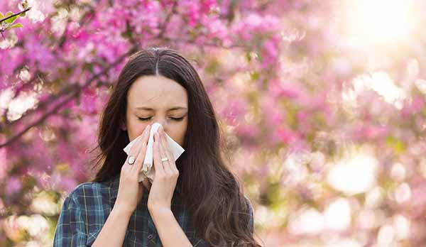 Young pretty girl blowing nose in front of blooming tree. Spring allergy concept