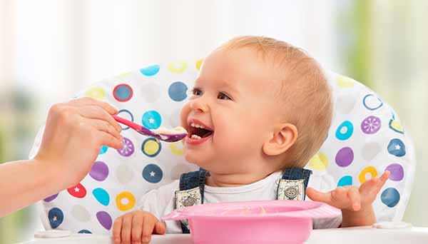 happy mother feeds funny baby from a spoon