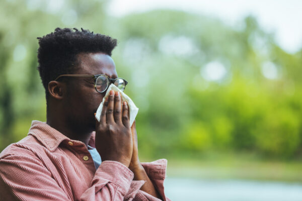 Allergic black man blowing on wipe in a park on spring season. M