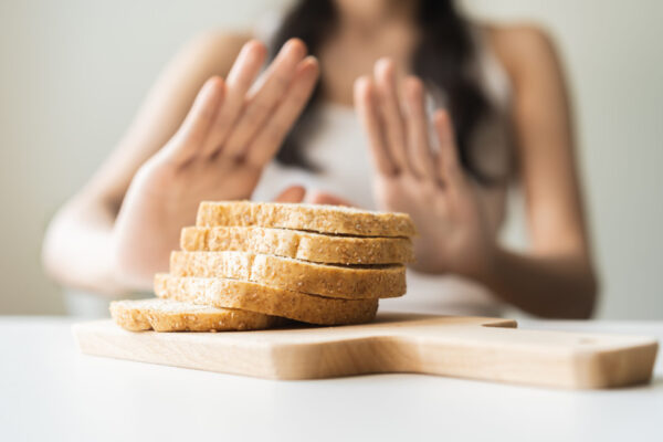 Gluten allergy, asian young woman hand push out, refusing to eat white bread slice on chopping board in food meal at home, girl having a stomach ache. Gluten intolerant and Gluten free diet concept.