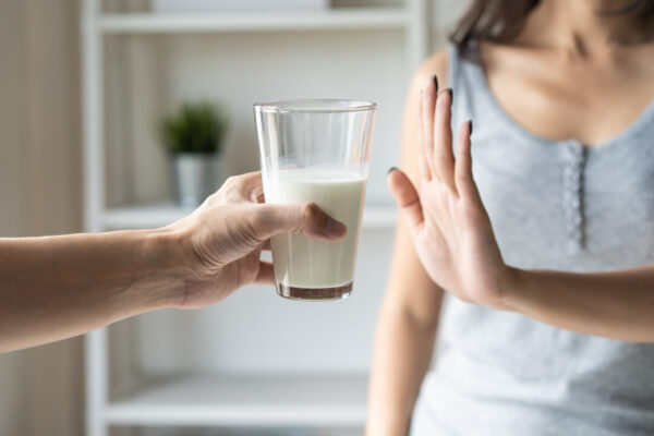 Close up of someone holding a glass of milk in front of a woman. She refuses to take it by holding her hand up in as if to say stop or no.