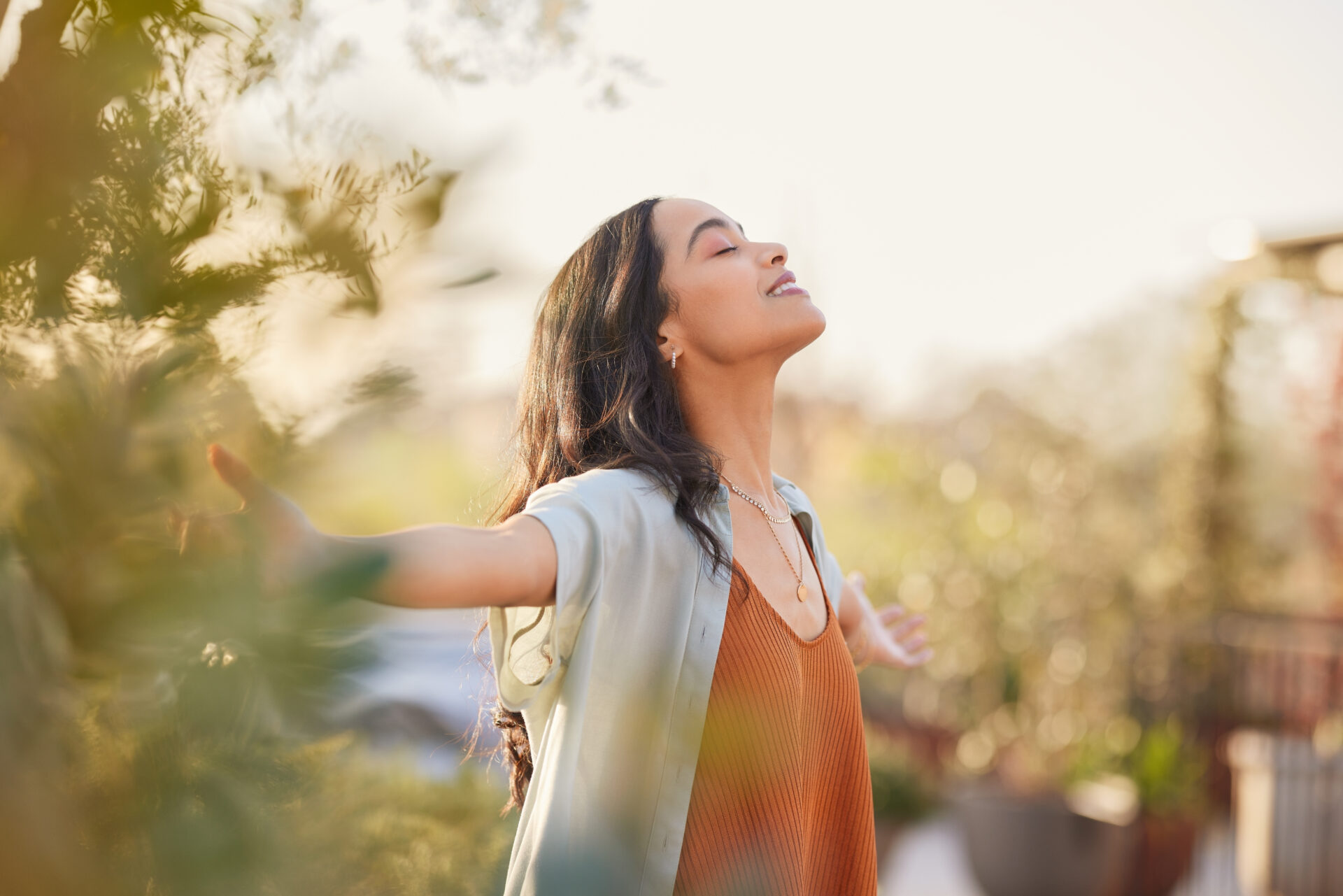 Woman standing outside with her arms stretched open and her eyes closed. She is breathing deeply.