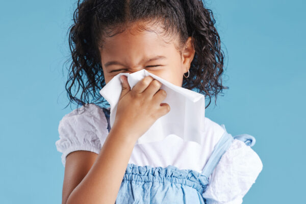 Young African-American girl in front of a blue background lowing her nose because of allergies