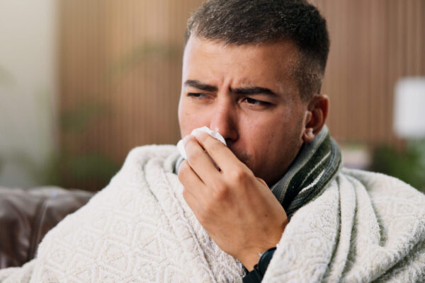 Closeup of a man on the couch wrapped in a blanket and suffering from severe allergies--depicting immune deficiency